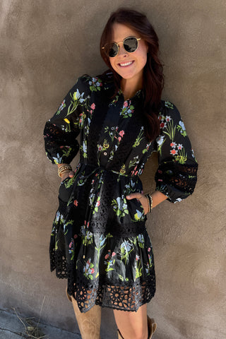Person lying on a concrete surface wearing a black floral dress.