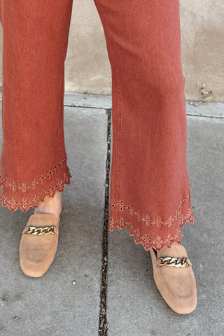 Person wearing high-waisted rust-colored jeans against a beige wall.