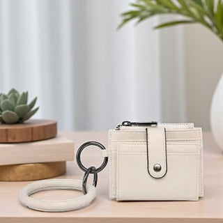 White wallet with keychain on a wooden surface with a plant in the background