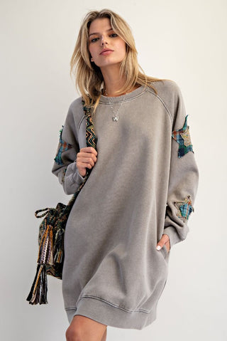 Woman wearing a gray sweatshirt dress with floral patterns on sleeves against a plain background