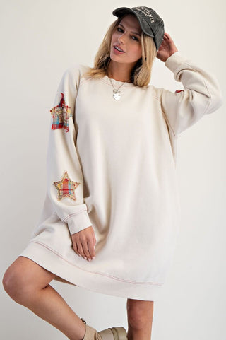 Woman wearing a cream-colored sweatshirt dress with star designs on a plain background