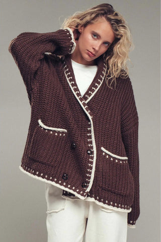 Woman wearing a brown knitted cardigan with white trim on a gray background