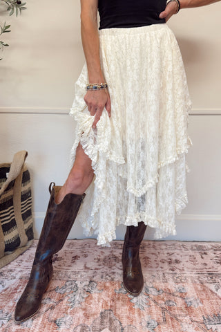 Person wearing a white lace skirt and brown boots on a patterned rug.