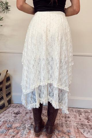 Person wearing a white lace skirt with brown boots on a patterned rug.